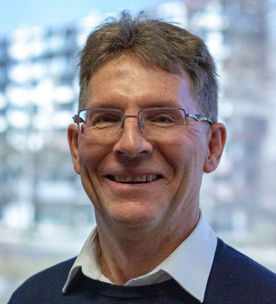 Man with short hair wearing glasses and a jumper over a shirt collar