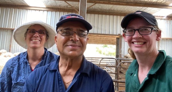 Two women and one man standing in a livestock shed and smiling