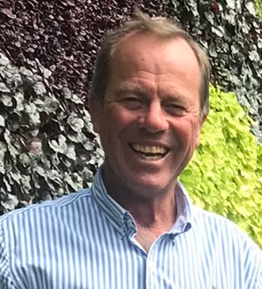 Man wearing blue and white checked shirt standing in front of greenery