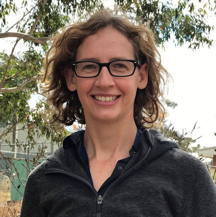 woman wearing a black shirt and glasses, smiling, with shoulder length hair